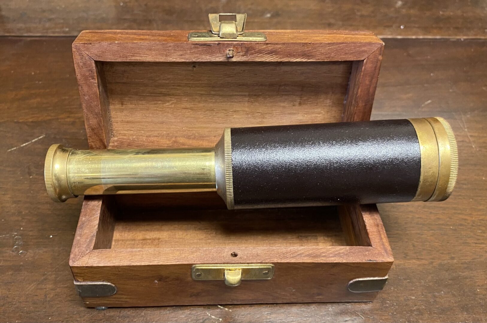 A telescope in its wooden case with the handle up.