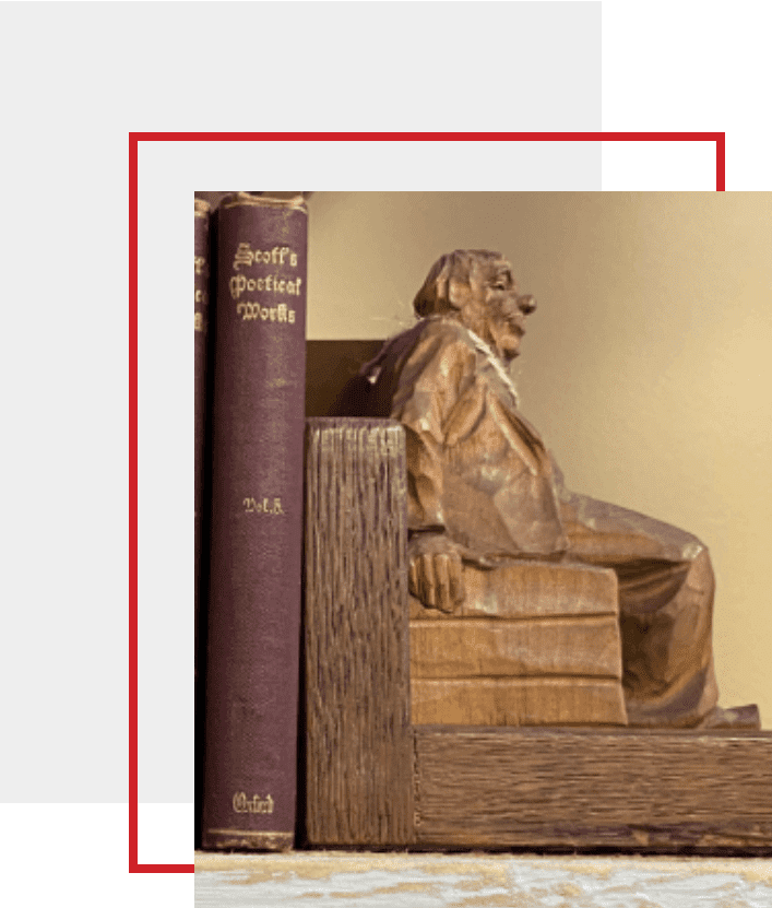 A wooden statue of a man sitting on top of books.