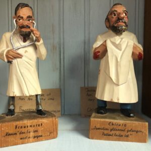 Two figurines of a man in white robes and glasses.