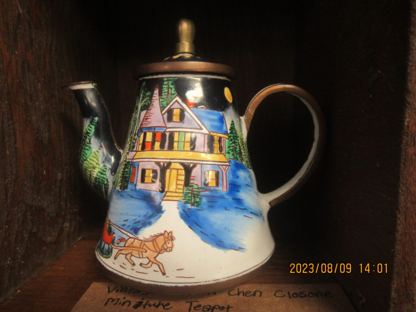 A tea pot with a picture of a house on it.