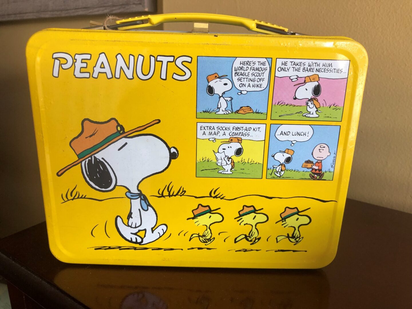 A yellow lunch box with peanuts cartoons on it.